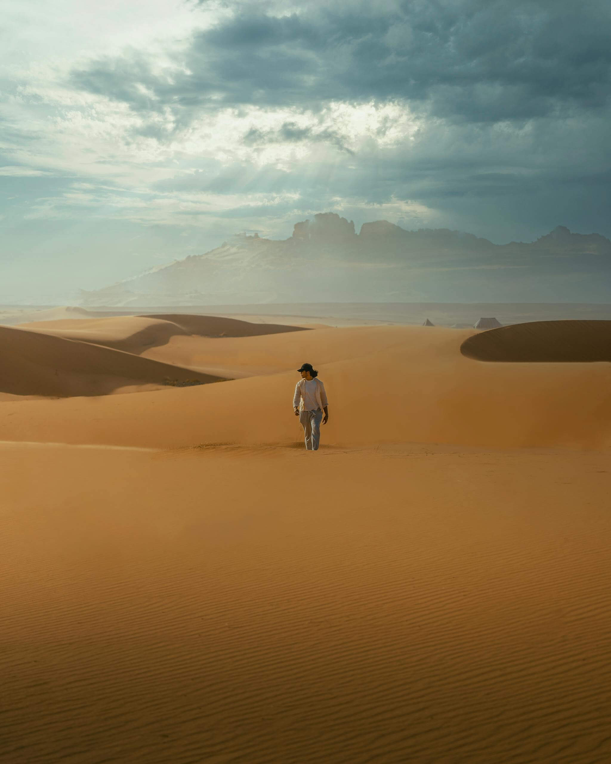 A lone traveler walks through the majestic sand dunes of Merzouga under a dramatic sky.