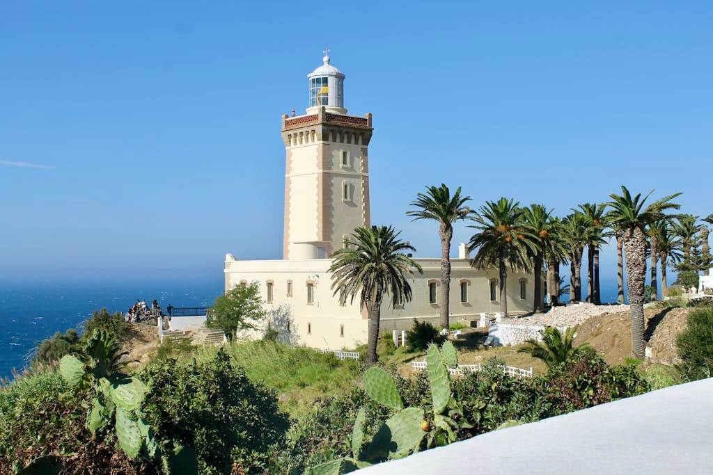 A scenic view of Cape Spartel Lighthouse surrounded by lush palm trees on a sunny day in Morocco.