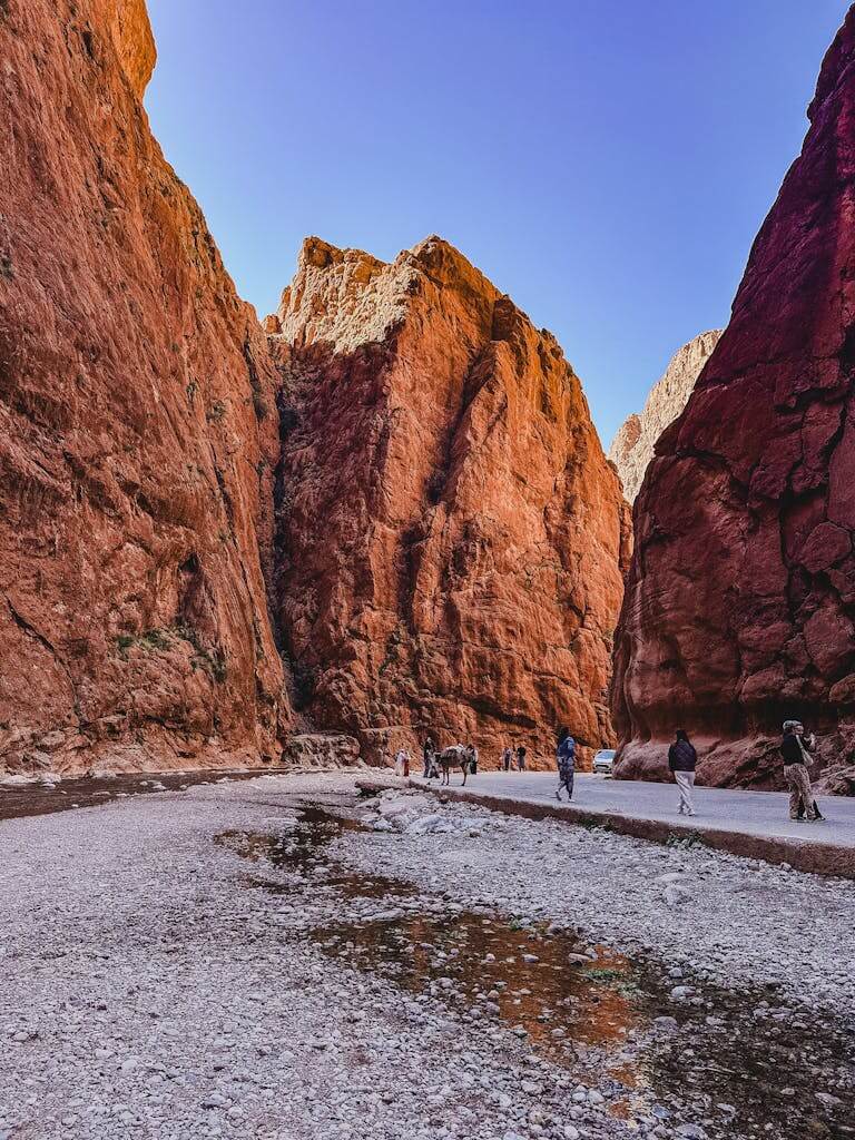 Sunlit red rock walls of Todra Gorge with people exploring the scenic path.