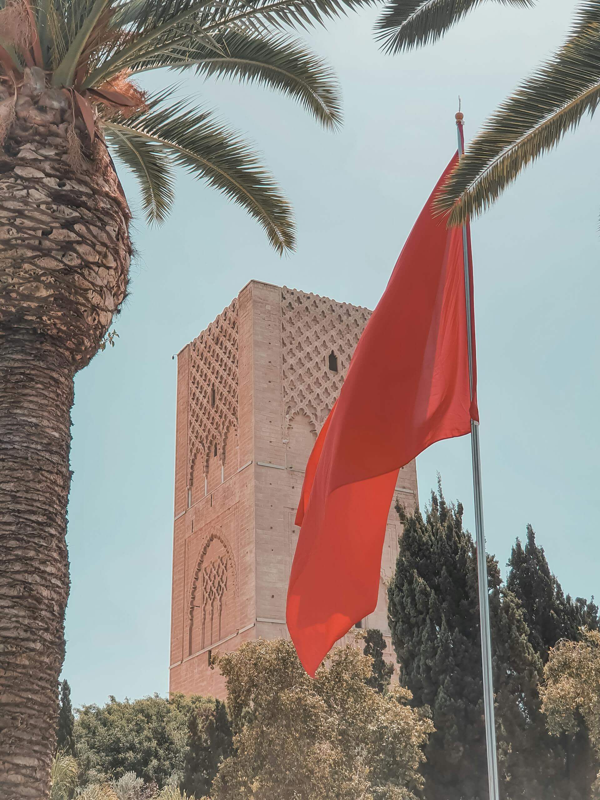 Capture of the iconic Hassan Tower with waving Moroccan flag and palm trees in Rabat.