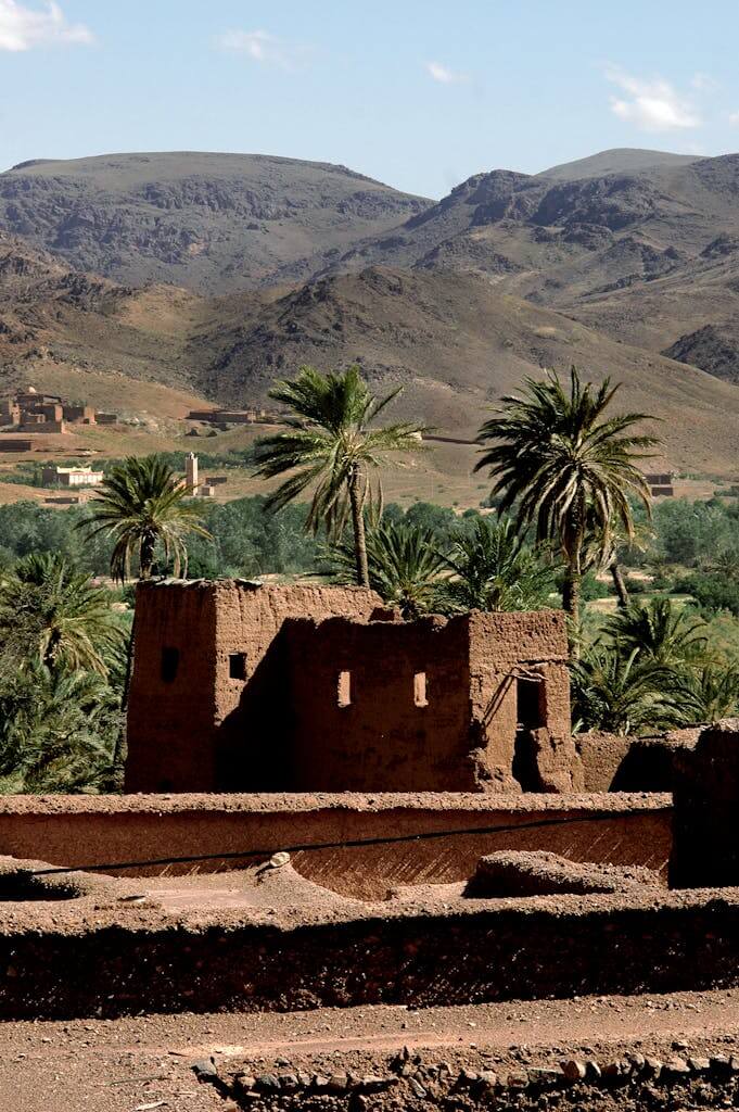 Historic Kasbah amidst palm trees and arid desert mountains in Ouarzazate, Morocco.